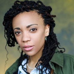 A woman with braided hair and a neutral expression against a blurred green background.
