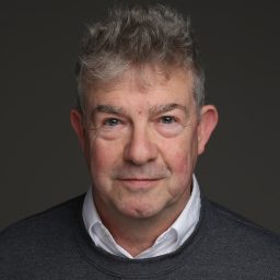 Robert Kitson wearing a dark suit and white shirt, smiling against a plain grey background.