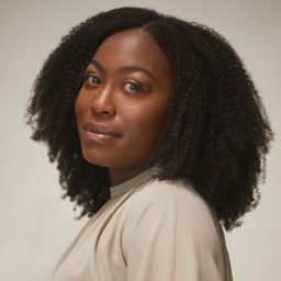 Stephanie Levi-John smiles, wearing a black top, against a blurred neutral background.