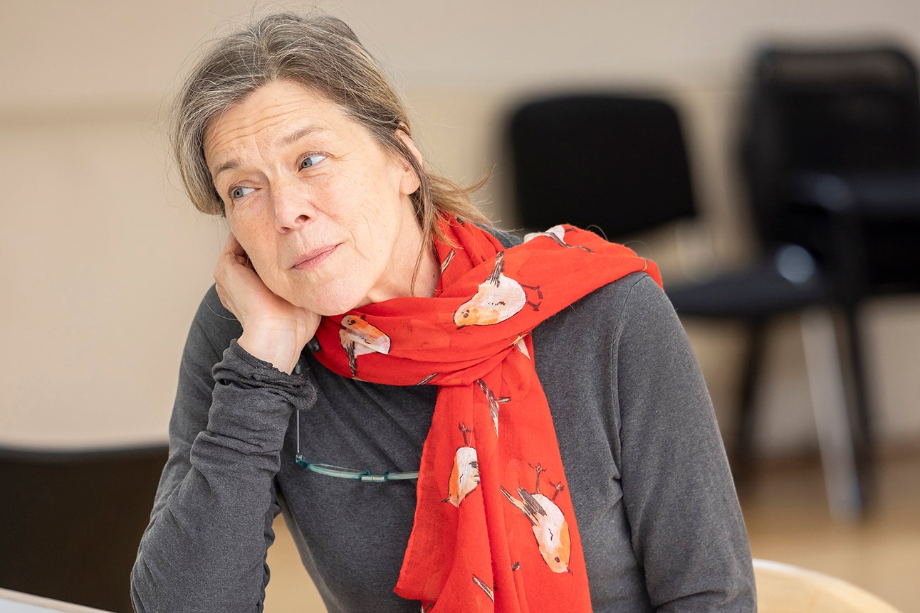 Woman with grey hair, wearing a red scarf, rests head on hand, thoughtful expression.