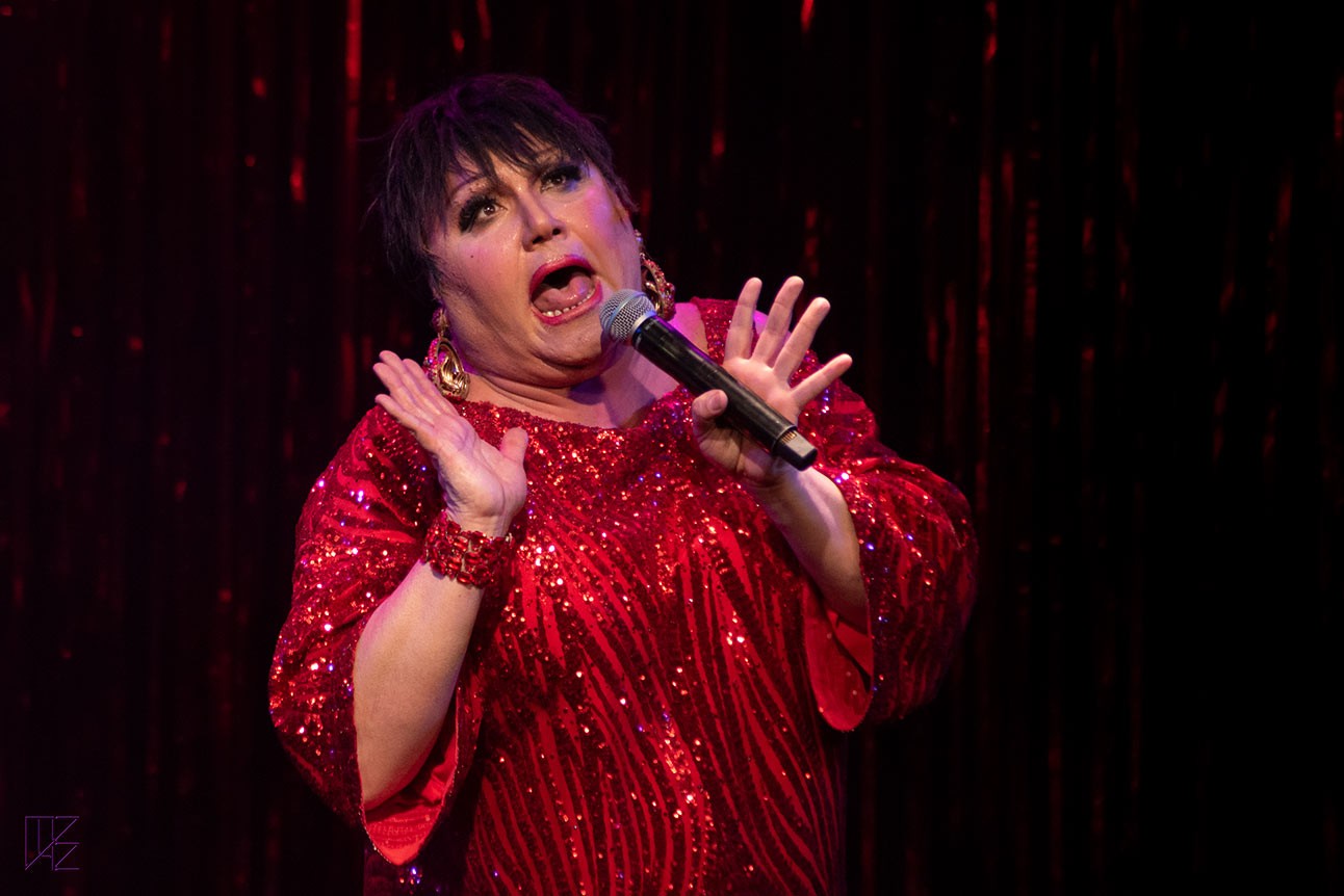Trevor Ashley singing on stage, against a dark background.