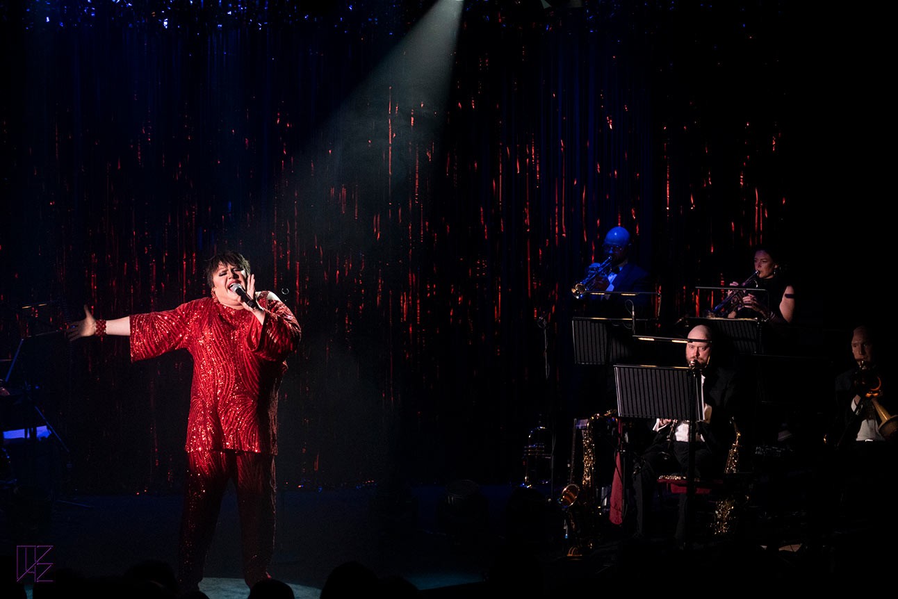 Trevor Ashley performs on stage with vibrant costumes and dramatic lighting.