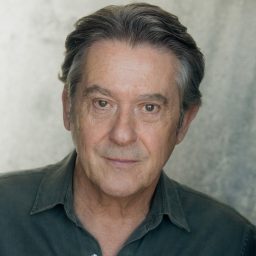 Adrian Lukis smiling, against a plain grey background.