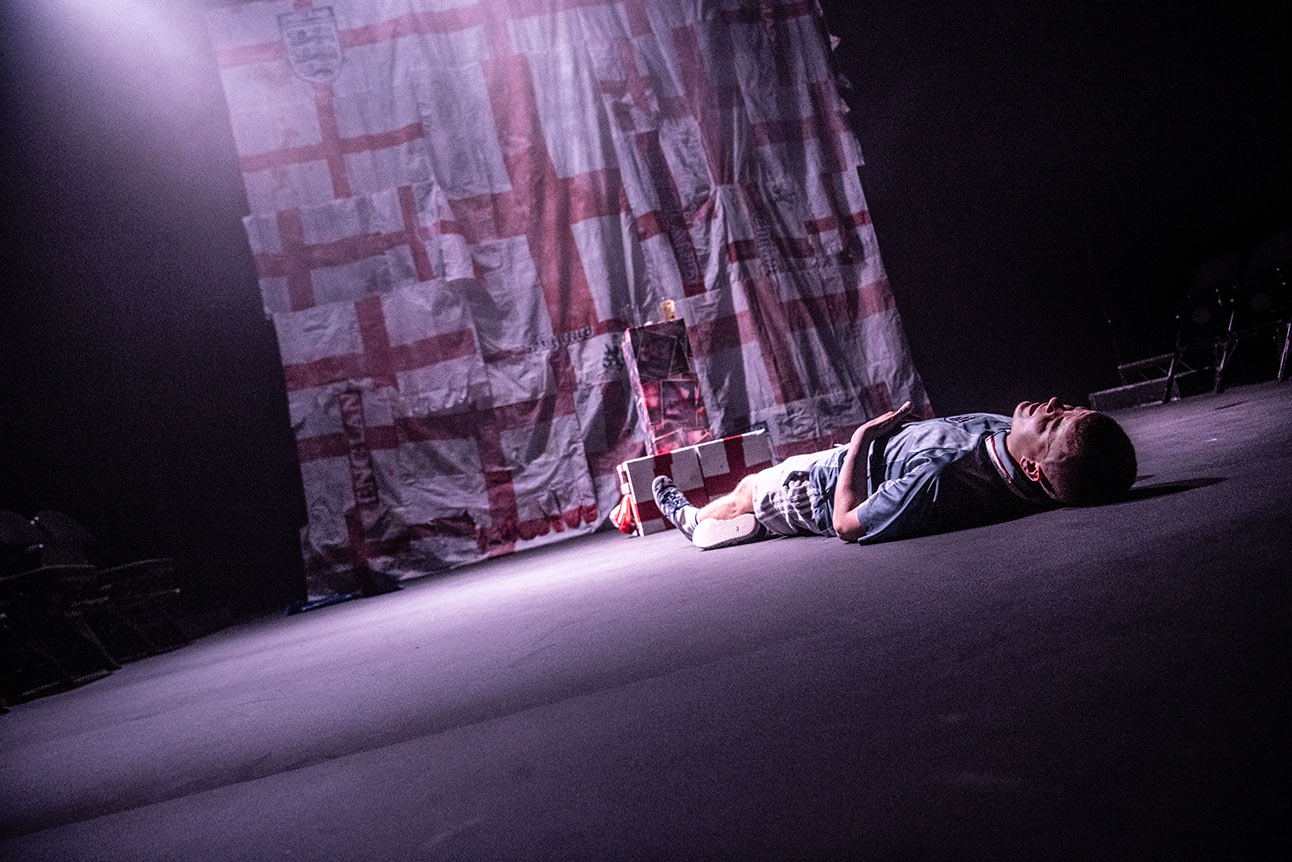 Man holding flare with smoke, wearing England football shirt, surrounded by cheering crowd in daylight.