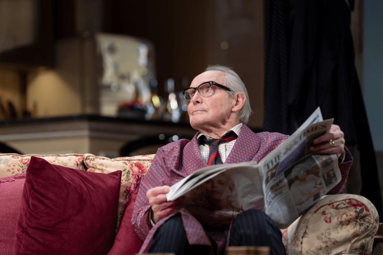 Sir Humphrey reads The Times in his dressing robe while sat on a sofa