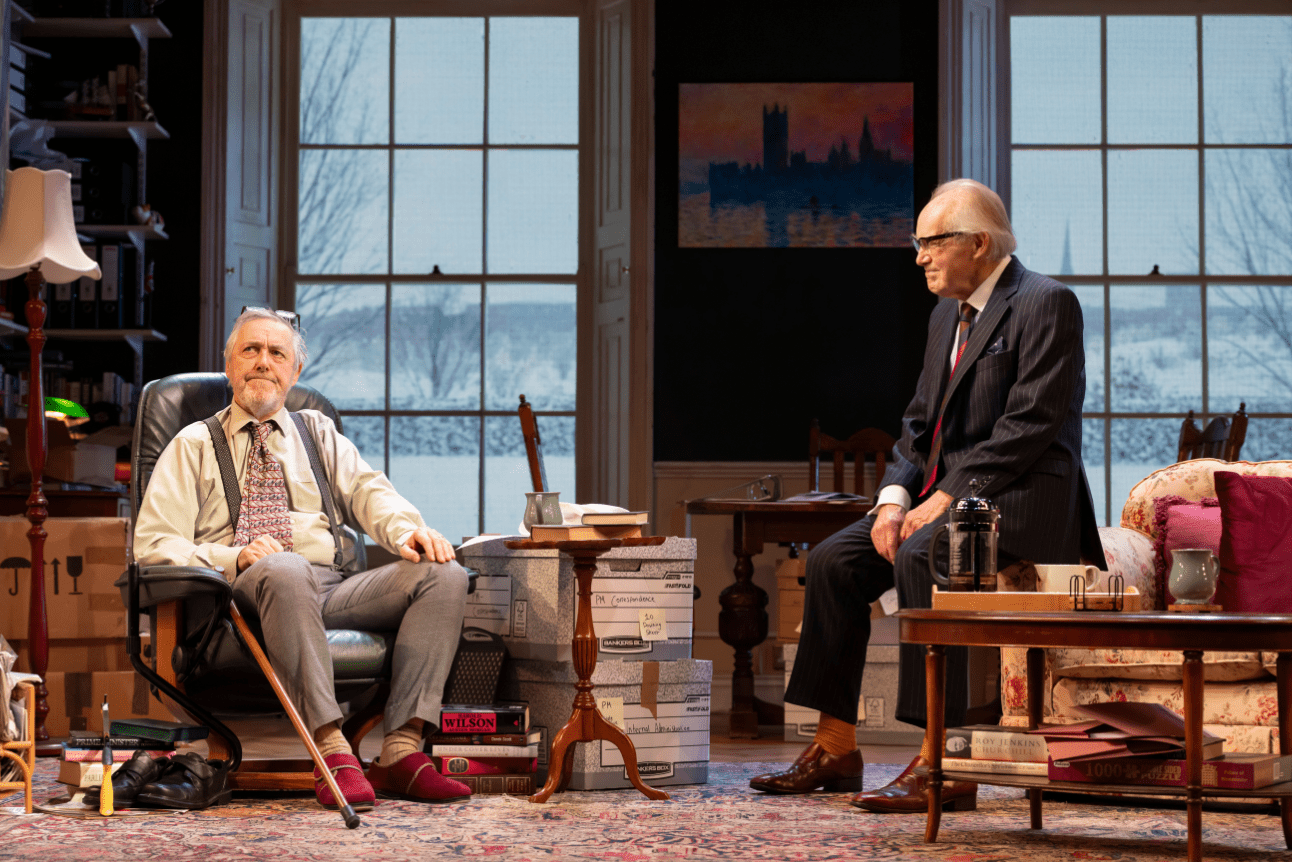 Jim Hacker and Sir Humphrey chat in a friendly manner while in Jim's study.