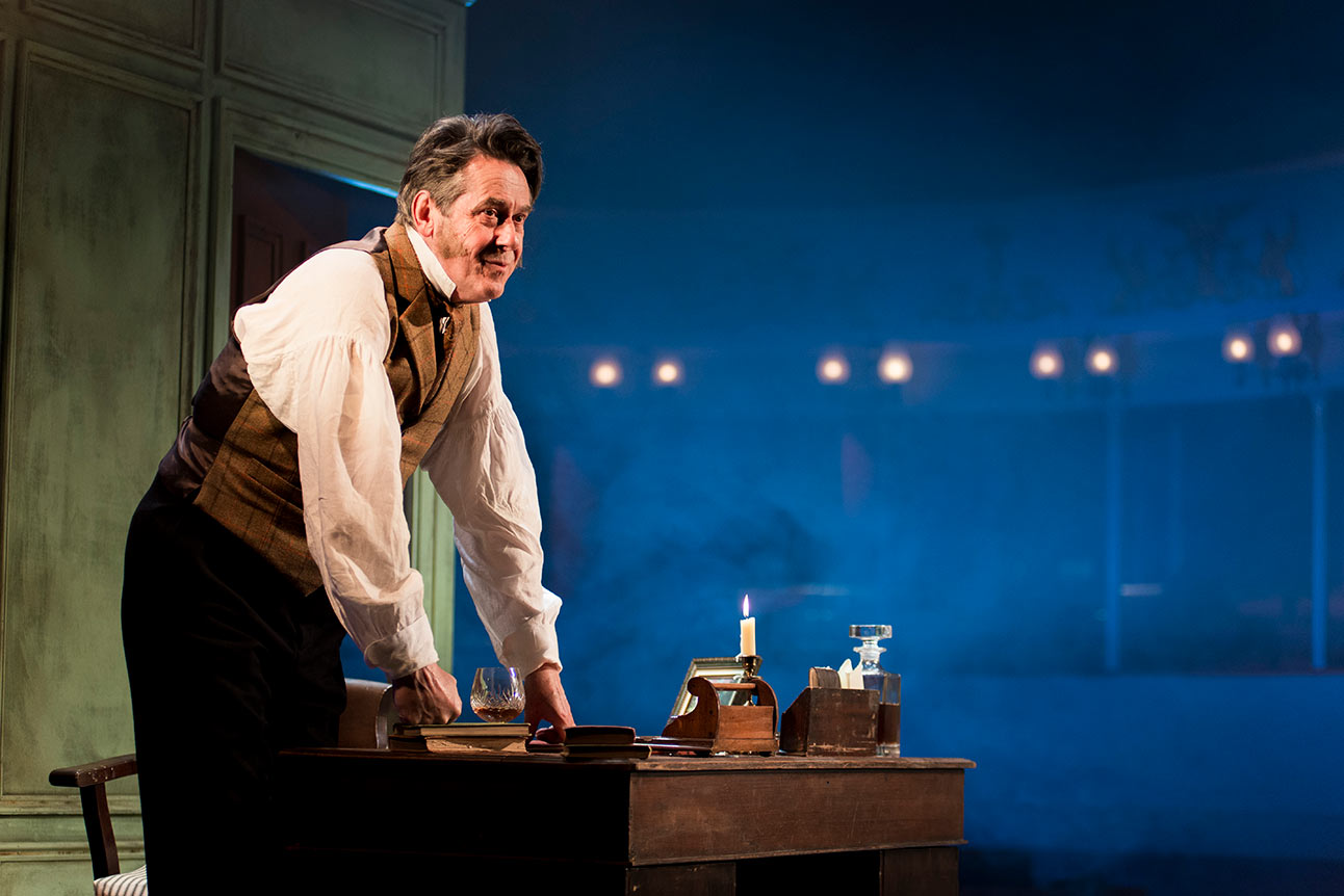 Adrian Lukis as Mr Wickham, wearing a period costume, stands on stage with a spotlight.