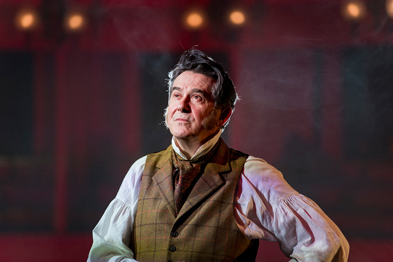 Adrian Lukis as Mr Wickham, wearing a period costume, stands on stage with a thoughtful expression.