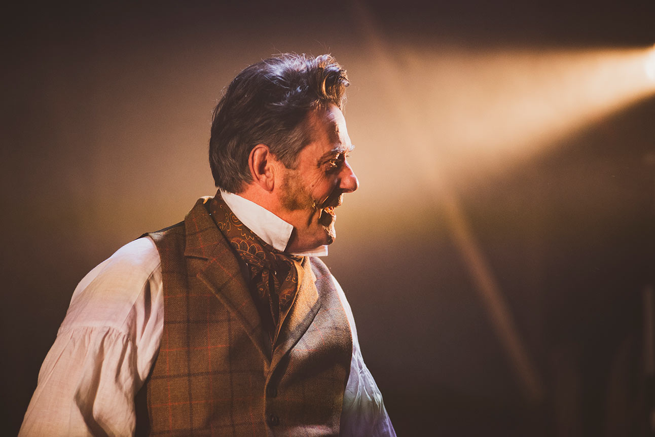 Adrian Lukis as Mr Wickham, wearing a period costume, stands on stage in profile.