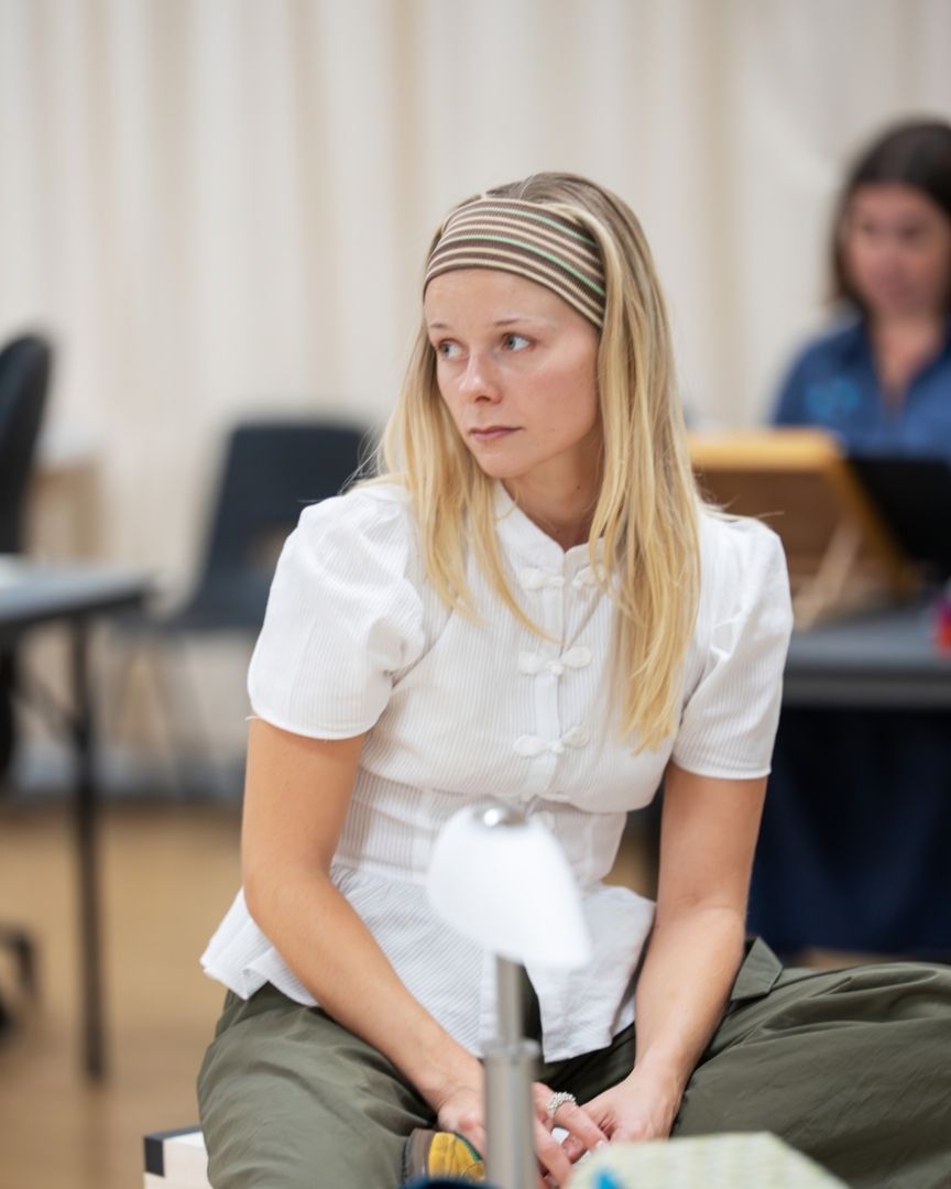 Phoebe Horn sits thoughtfully, wearing a white blouse and headband