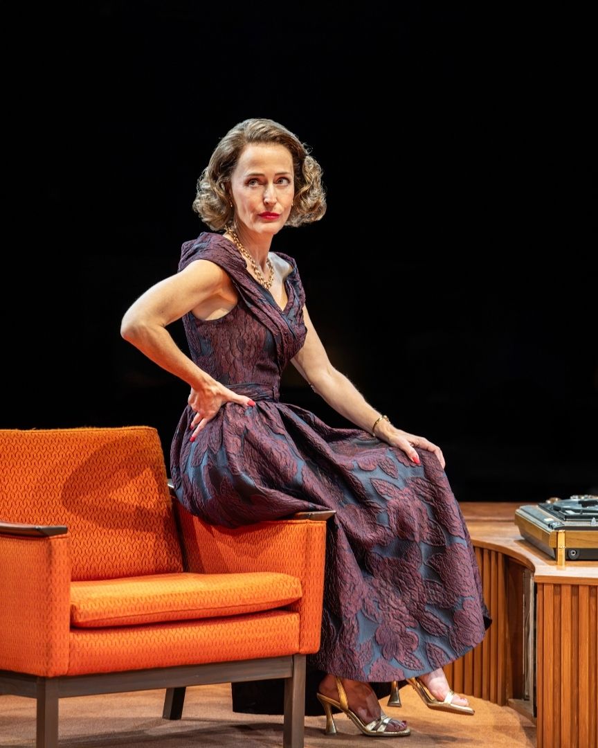 A woman in a purple dress sits on an orange chair, with a record player nearby.
