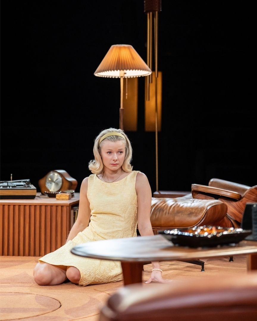 Woman in yellow dress sits on floor, vintage decor with lamp and radio in background.