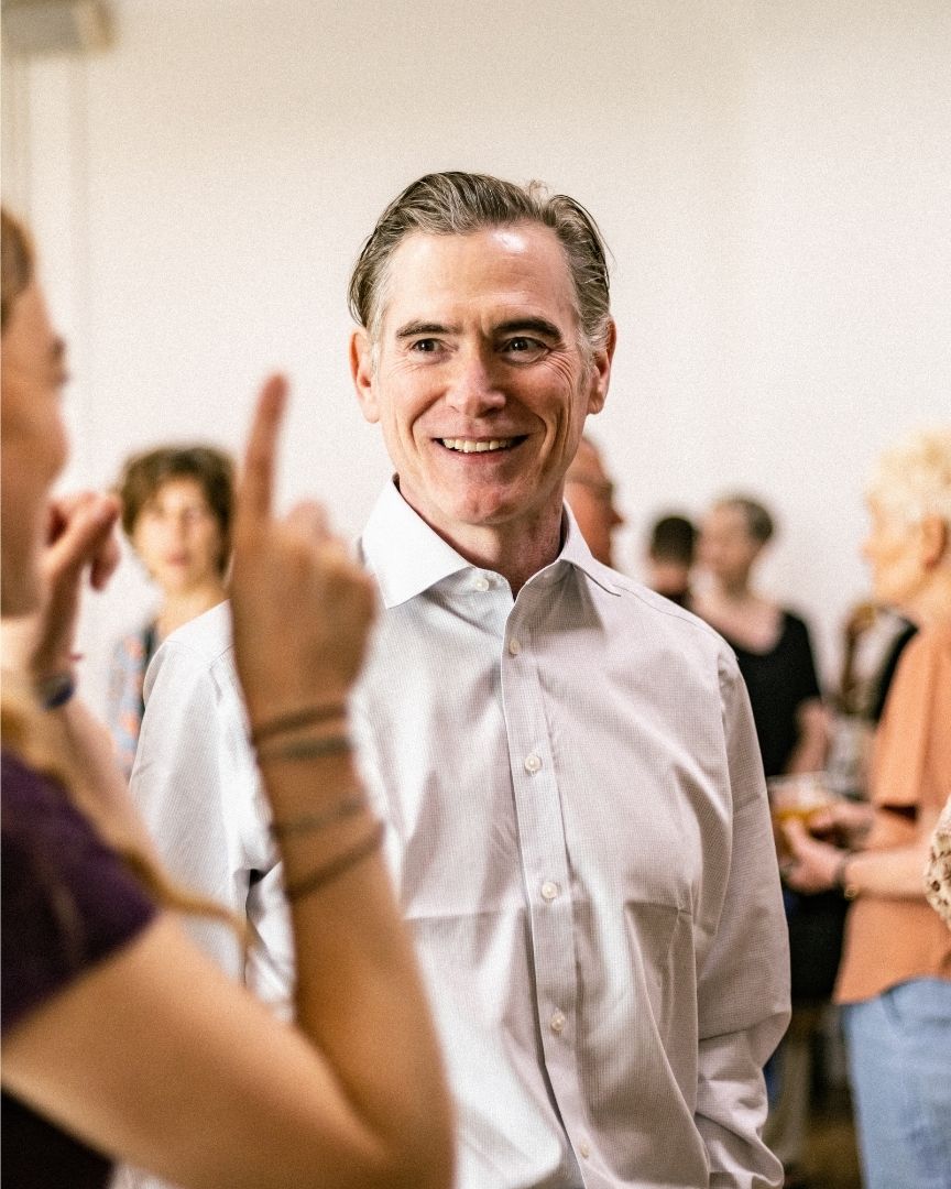 A man in a white shirt smiles while engaging in conversation at a social gathering.