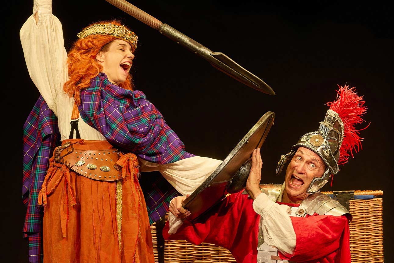 Two actors in historical costumes, one wielding a spear, the other in Roman armour, performing.