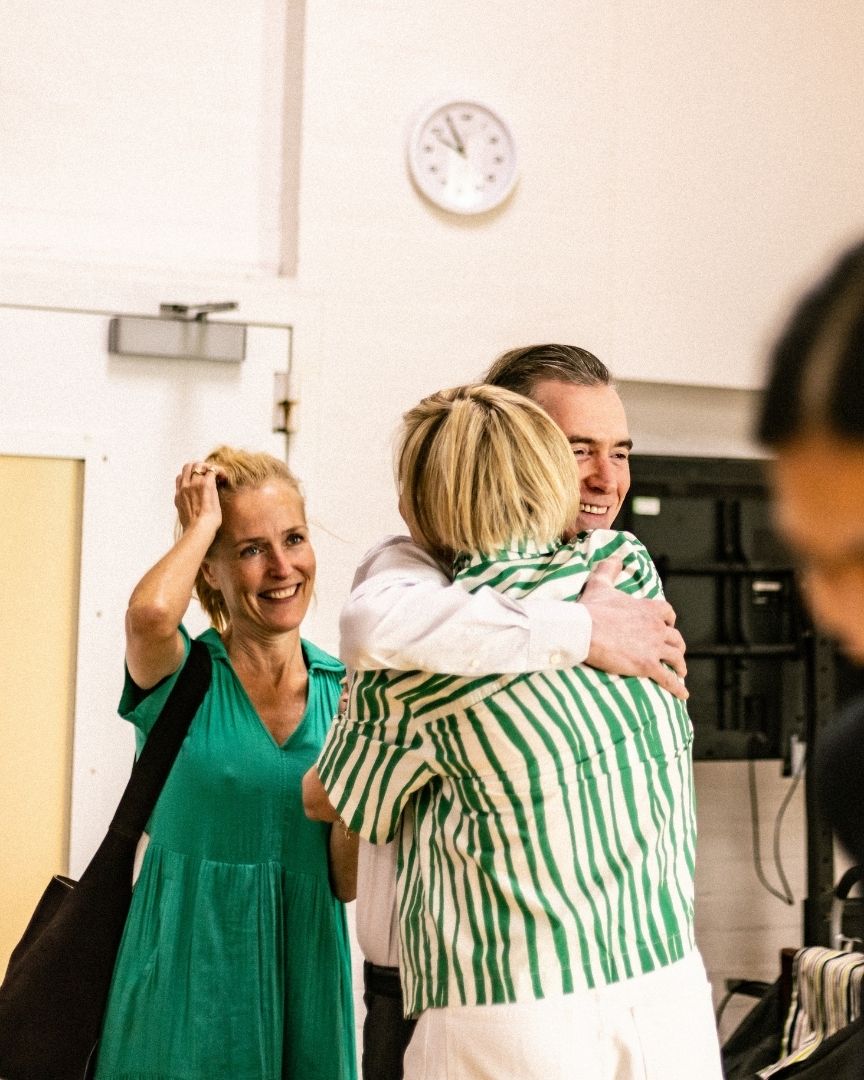 Two people embrace warmly, while a woman in a green dress smiles nearby.