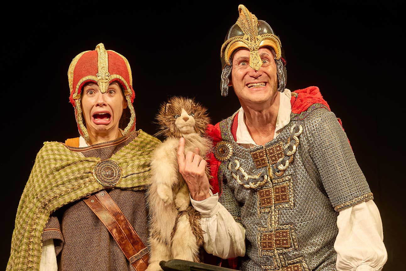 Two actors in medieval costumes, one holding a puppet, expressively performing on stage.