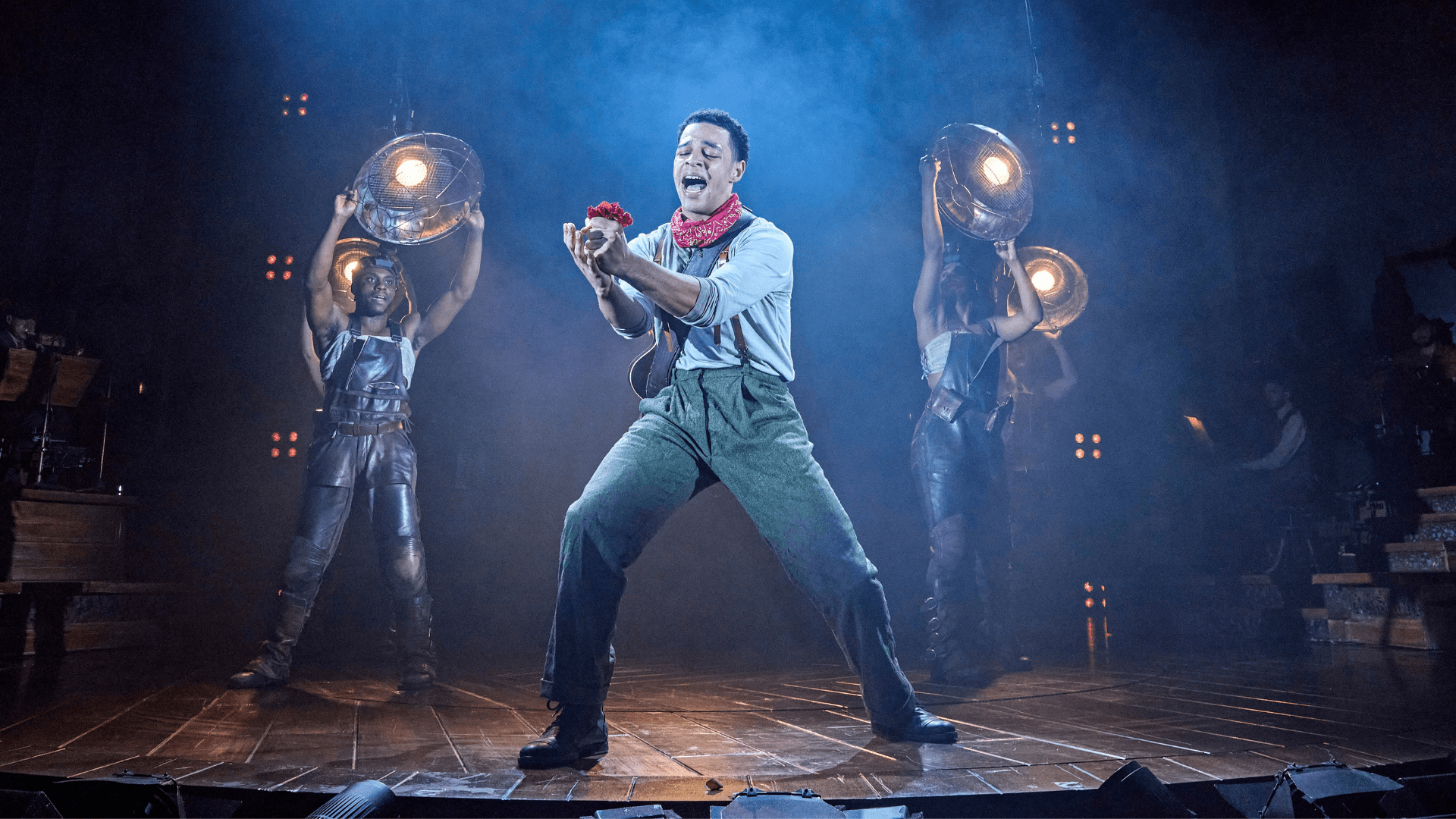 Hadestown Orpheus sings out passionately while holding out a bright red flower