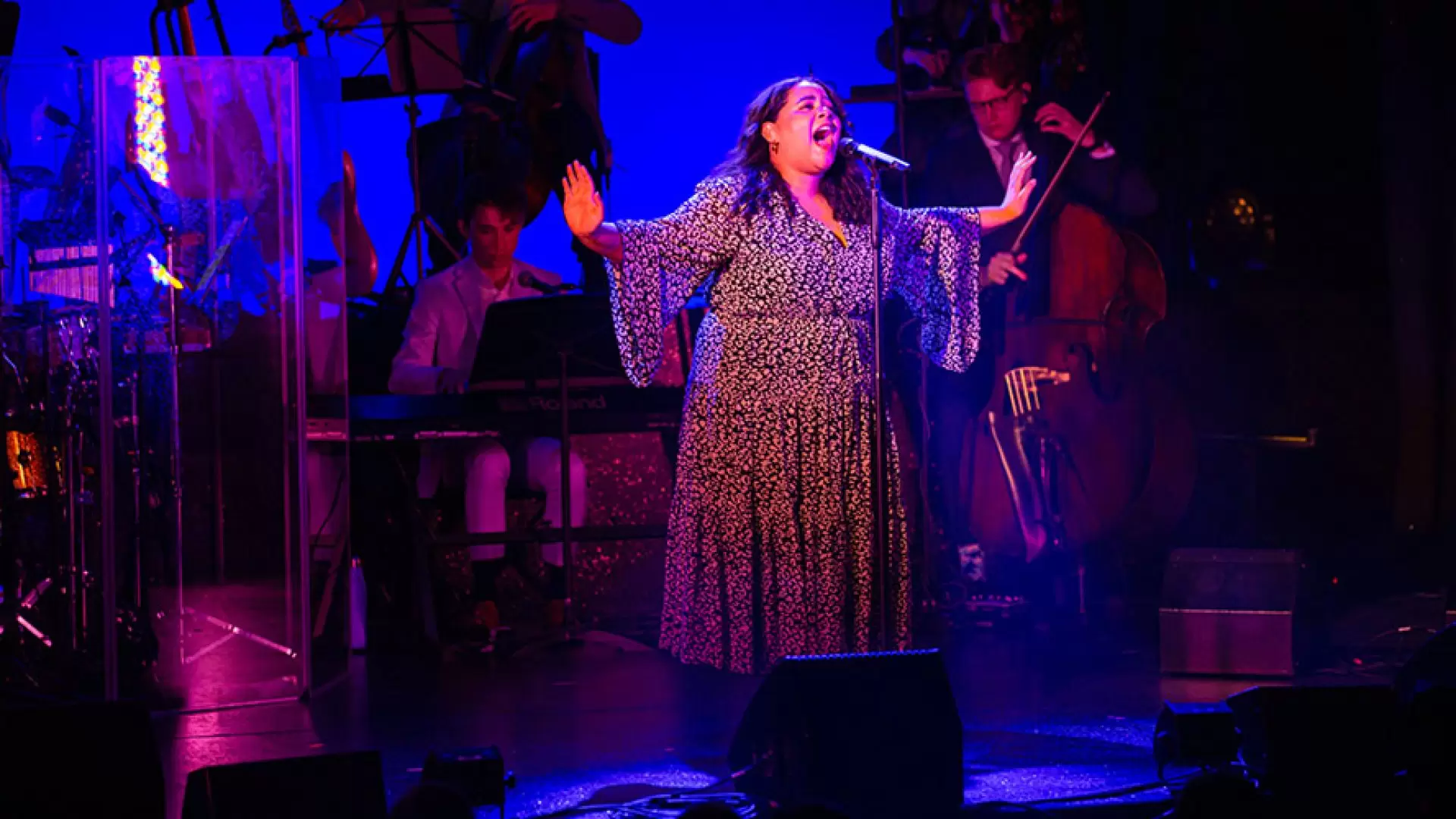 Two actors on stage, one kneeling, one standing, both in casual attire, with a dark backdrop.