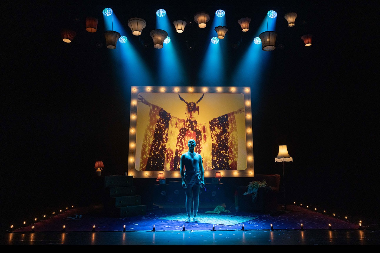 Rob Madge stands centre stage under blue lights, with a colourful backdrop and vintage decor.