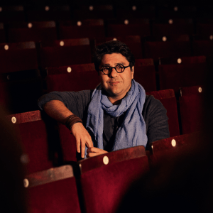 Nassim Soleimanpour with glasses and a blue scarf sits in the Duchess Theatre Auditorium.