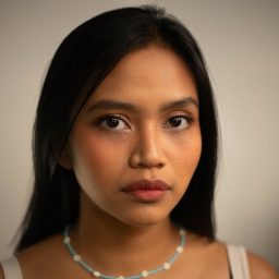 A woman with long black hair and a pearl necklace, gazing directly at the camera.