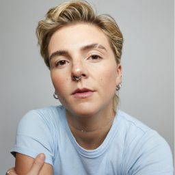 Person with short blonde hair wearing a light blue shirt, looking directly at the camera.