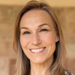 Joanna Riding, smiling wearing a patterned top, standing against a blurred background.