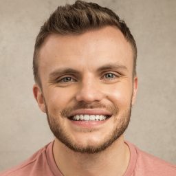 Smiling man with short hair wearing a pink shirt against a beige background.