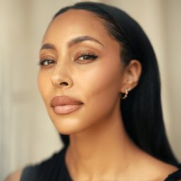A person with long dark hair, wearing earrings, looks confidently at the camera against a neutral background.