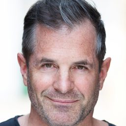 Michael Matus with short grey hair smiles slightly, wearing a dark top against a blurred background.