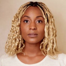 Sydney Sainte looks at the camera with a neutral expression, against a plain beige background.