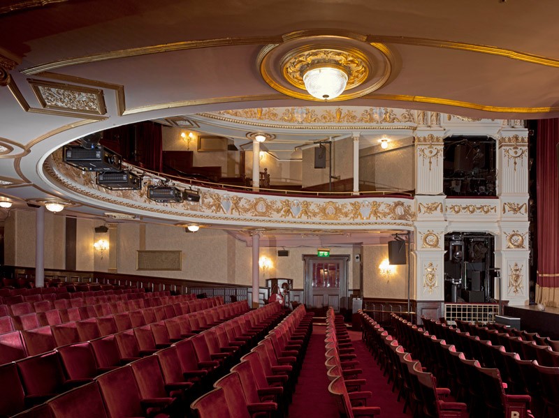 Interior of The Garrick Theatre, featuring red seats, ornate balconies, and a decorative ceiling light.