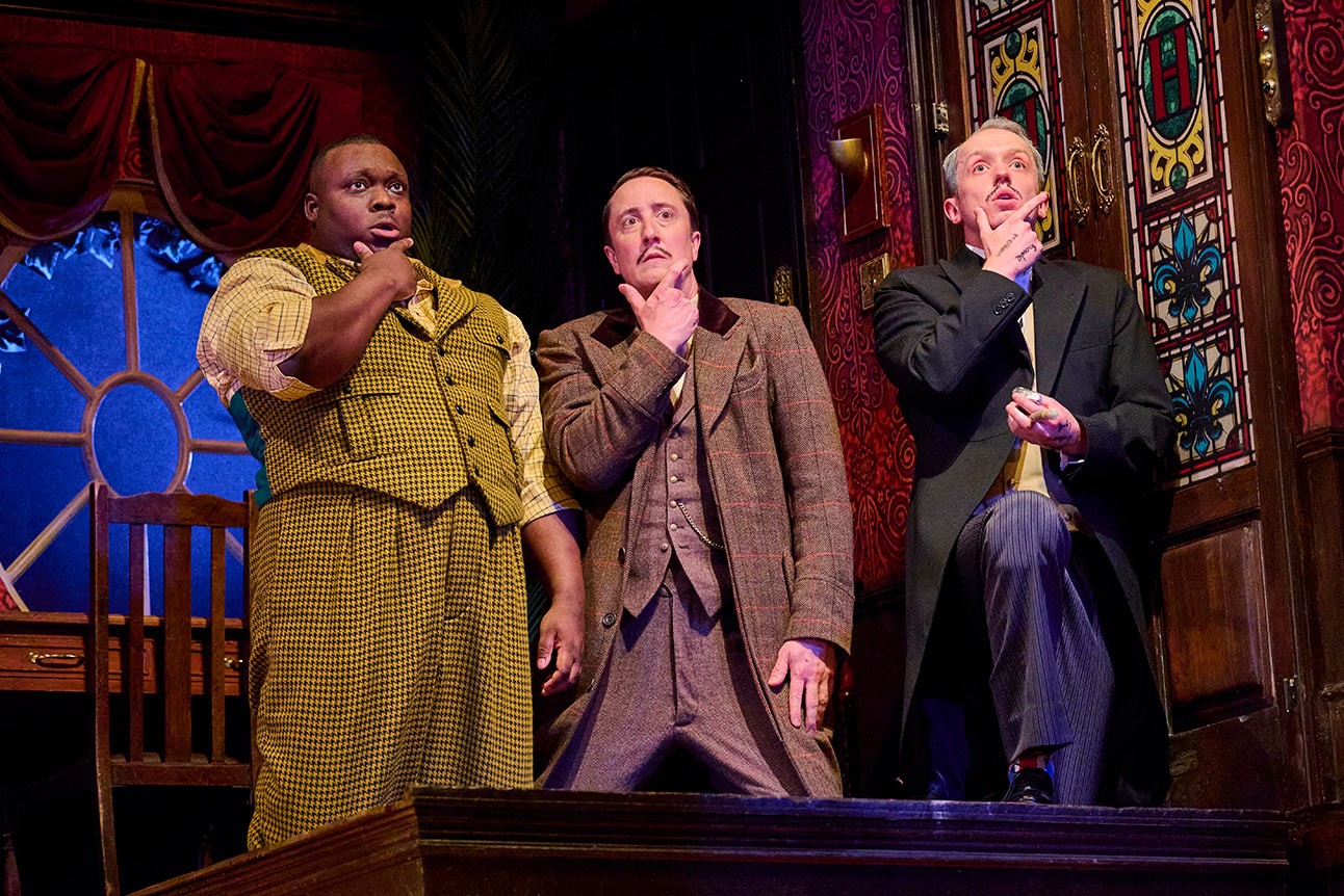 Raphael Bushay, Matthew Spencer, and Alex Bird on stage, posing thoughtfully with hands on chins.