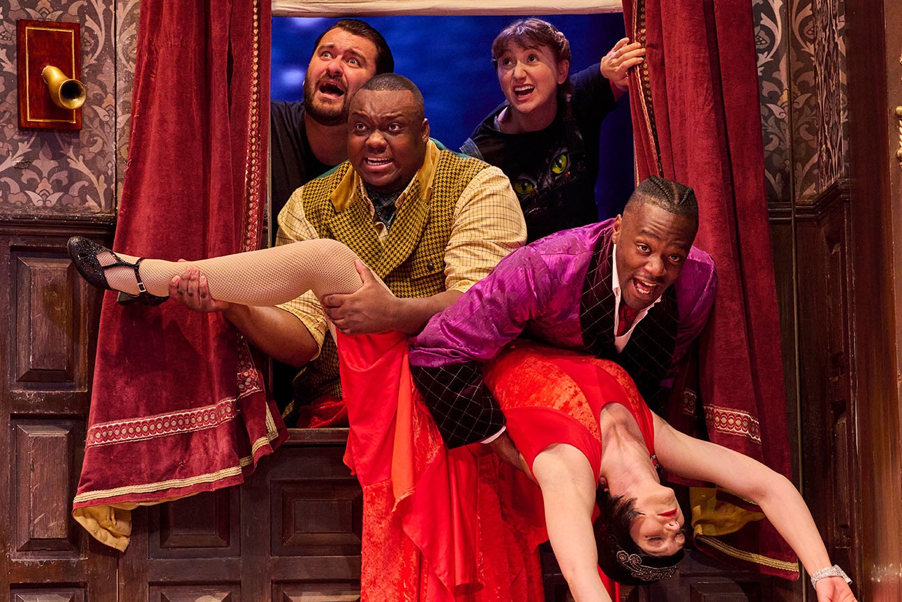 Four actors in colourful costumes perform a comedic scene with dramatic expressions and dynamic poses.