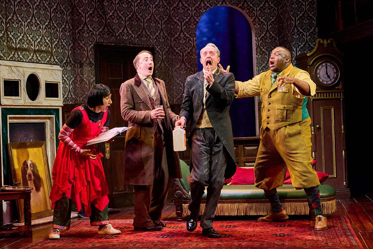Four actors in period costumes perform dramatically on stage with ornate wallpaper and furniture.