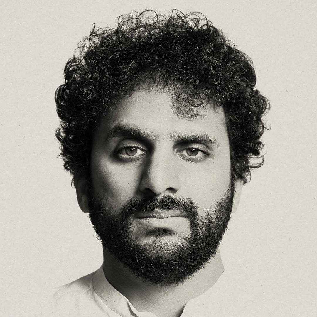 A person with curly hair and a beard looks directly at the camera against a plain background.