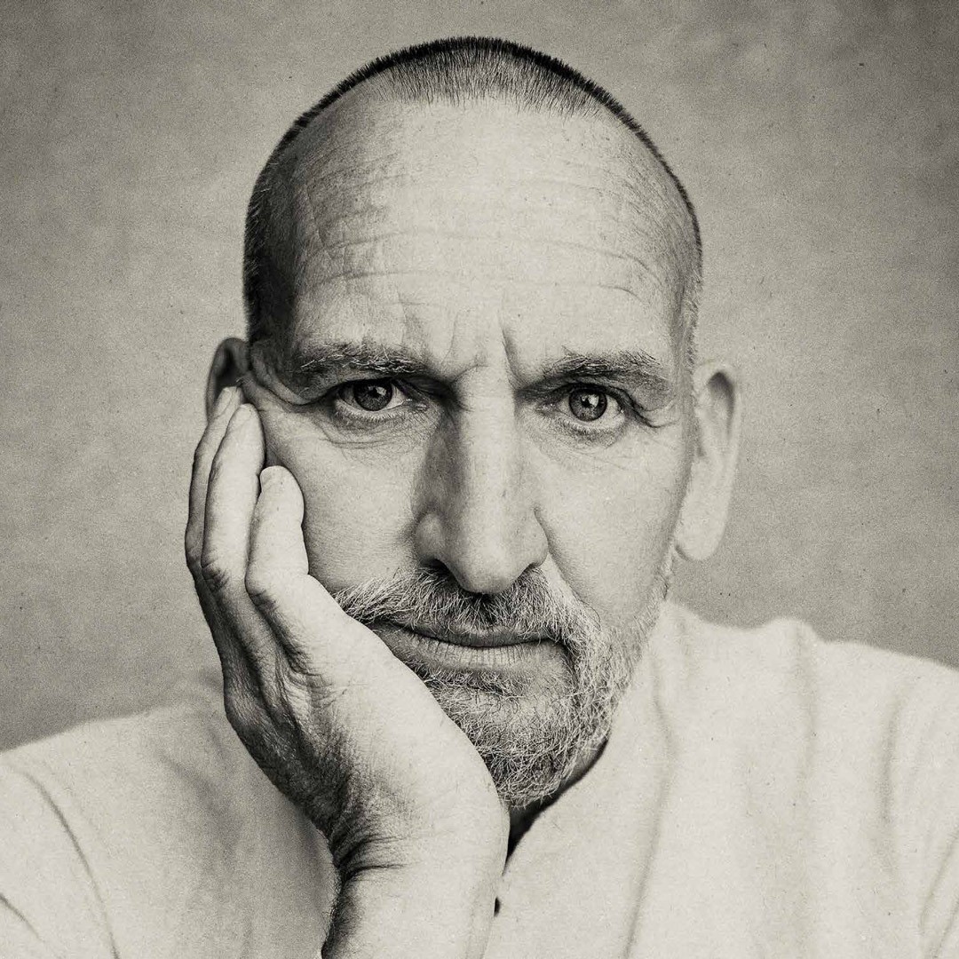 Bald man with hand on chin, wearing light shirt, neutral expression, textured grey background.