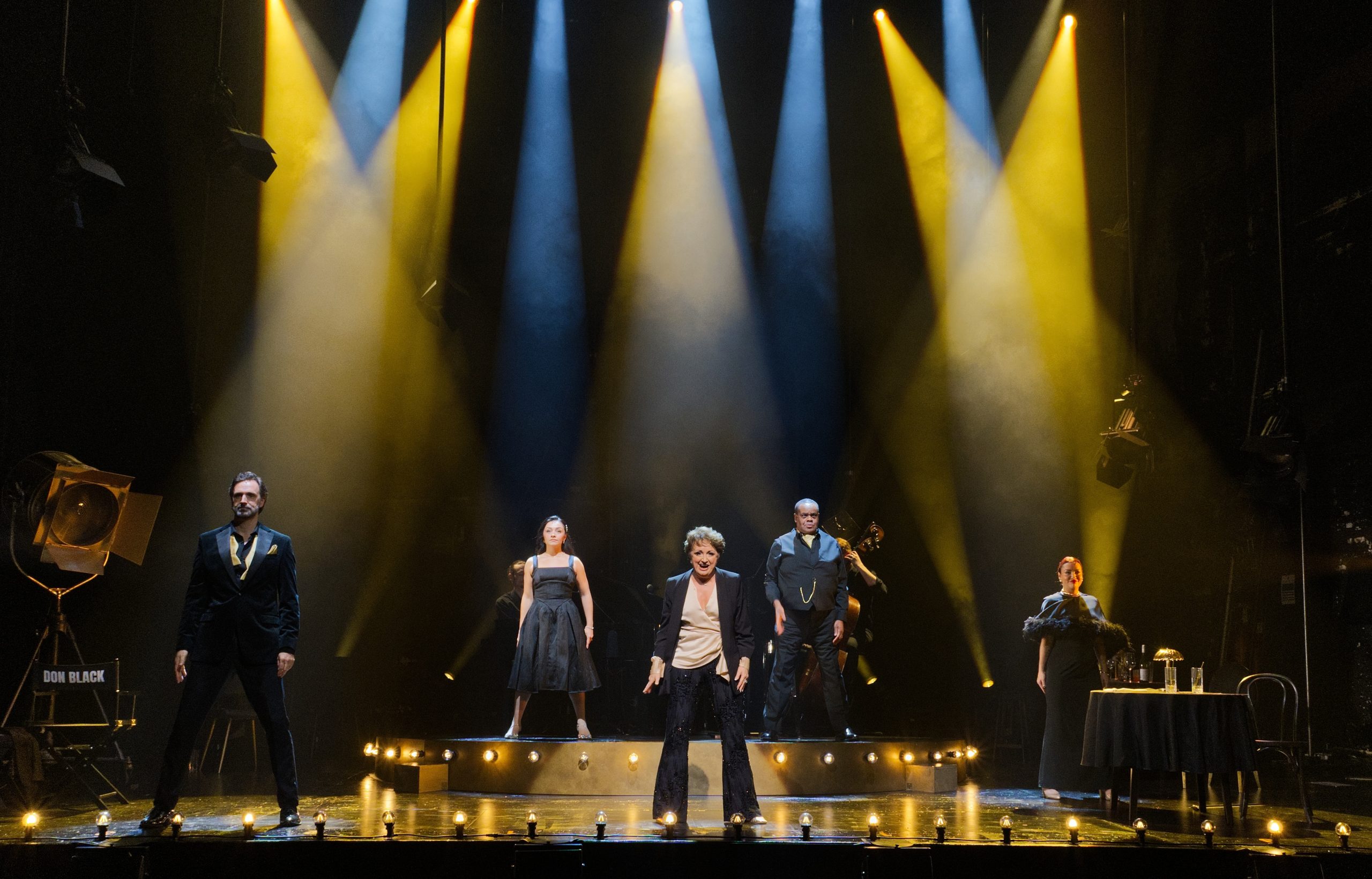 Performers on stage under yellow and blue lights at Garrick Theatre, wearing formal attire.