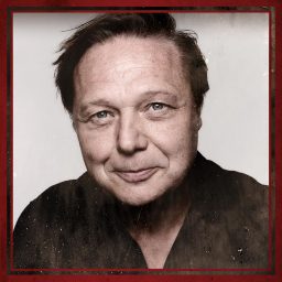 A man with short hair and a slight smile, framed in a red-bordered square.