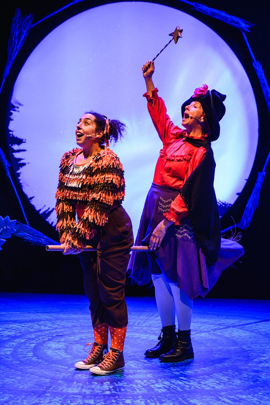 Two performers on stage; one dressed as a cat, the other as a witch on a broom.