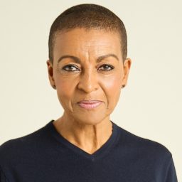 A woman with short hair, wearing a dark top, poses against a plain light background.