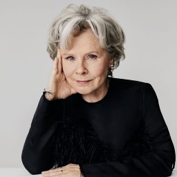 Imelda Staunton poses with hand on face, wearing a black top against a grey background.