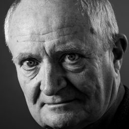 Black and white portrait of an older man with short hair, looking directly at the camera.