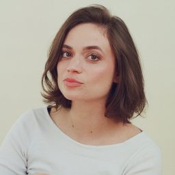 A woman with short brown hair wearing a white top, against a plain light background.