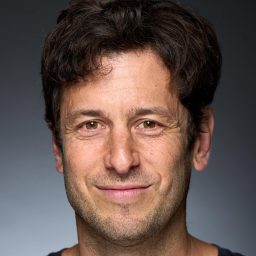 Smiling man with dark hair against a grey background.