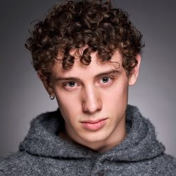 Young man with curly hair wearing a grey hoodie, looking directly at the camera.