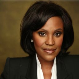 A woman with shoulder-length dark hair, wearing a black blazer and white shirt, smiles softly.