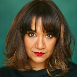 A woman with shoulder-length brown hair and red lipstick against a green background.