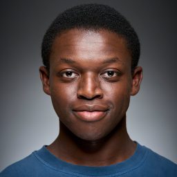 A person wearing a blue shirt, smiling slightly, against a grey gradient background.