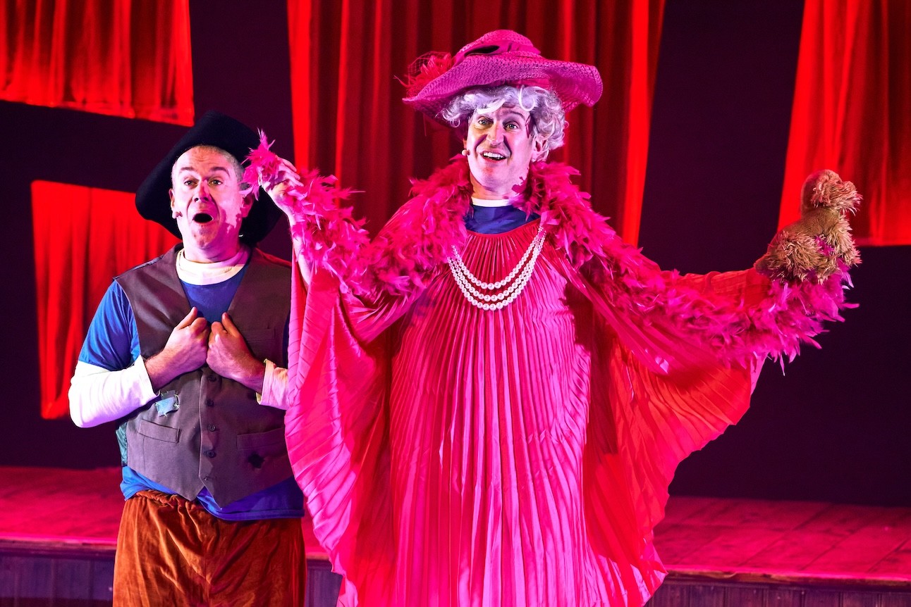 Potted Panto actors in colourful costumes, holding a prop, performing on stage at Wilton's Music Hall.